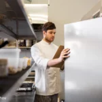 Koch macht mit Klemmbrett Kontrolle der Kühlschranktemperatur um die Lebensmittelsicherheit zu gewährleisten - PJ5MNSQ - Foto dolgachov